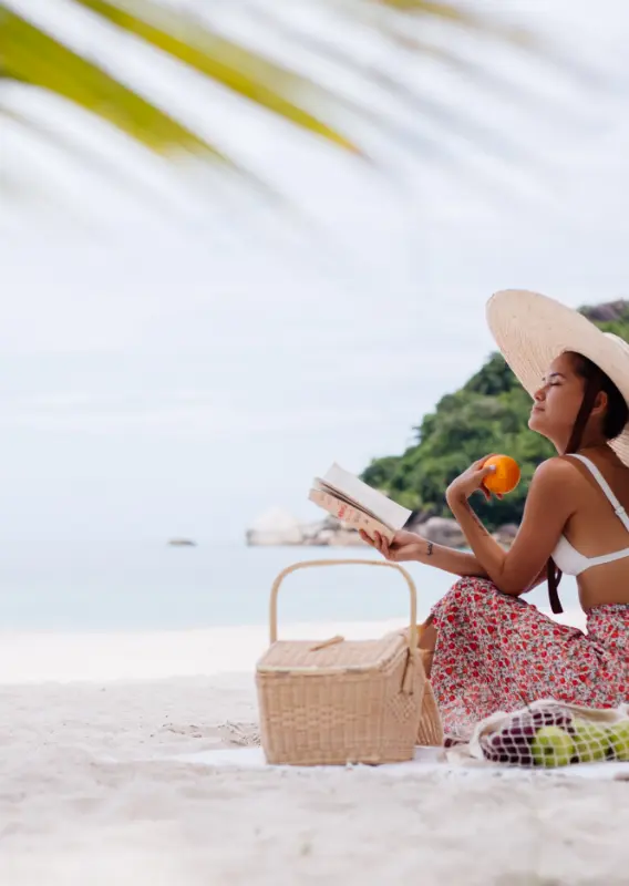 Joven tomándose una bebida y leyendo un libro en la playa